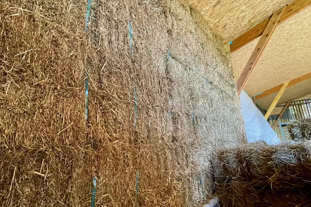 Muro de balas de paja apiladas contra la estructura de madera de la bodega de almacenamiento del Domaine des Cinq Autels