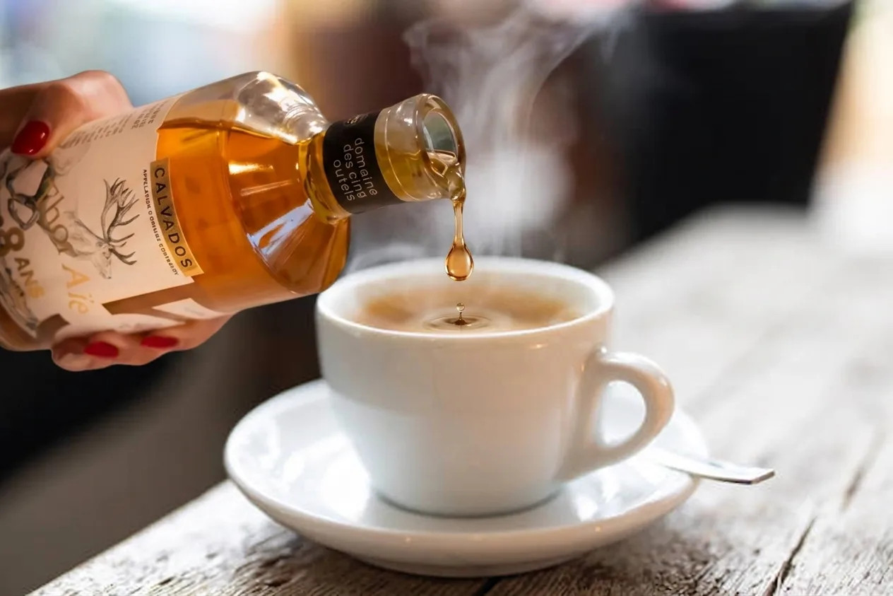 Calvados Thor Aïe del Domaine des Cinq Autels vertido en una taza de café humeante, sobre una mesa de madera
