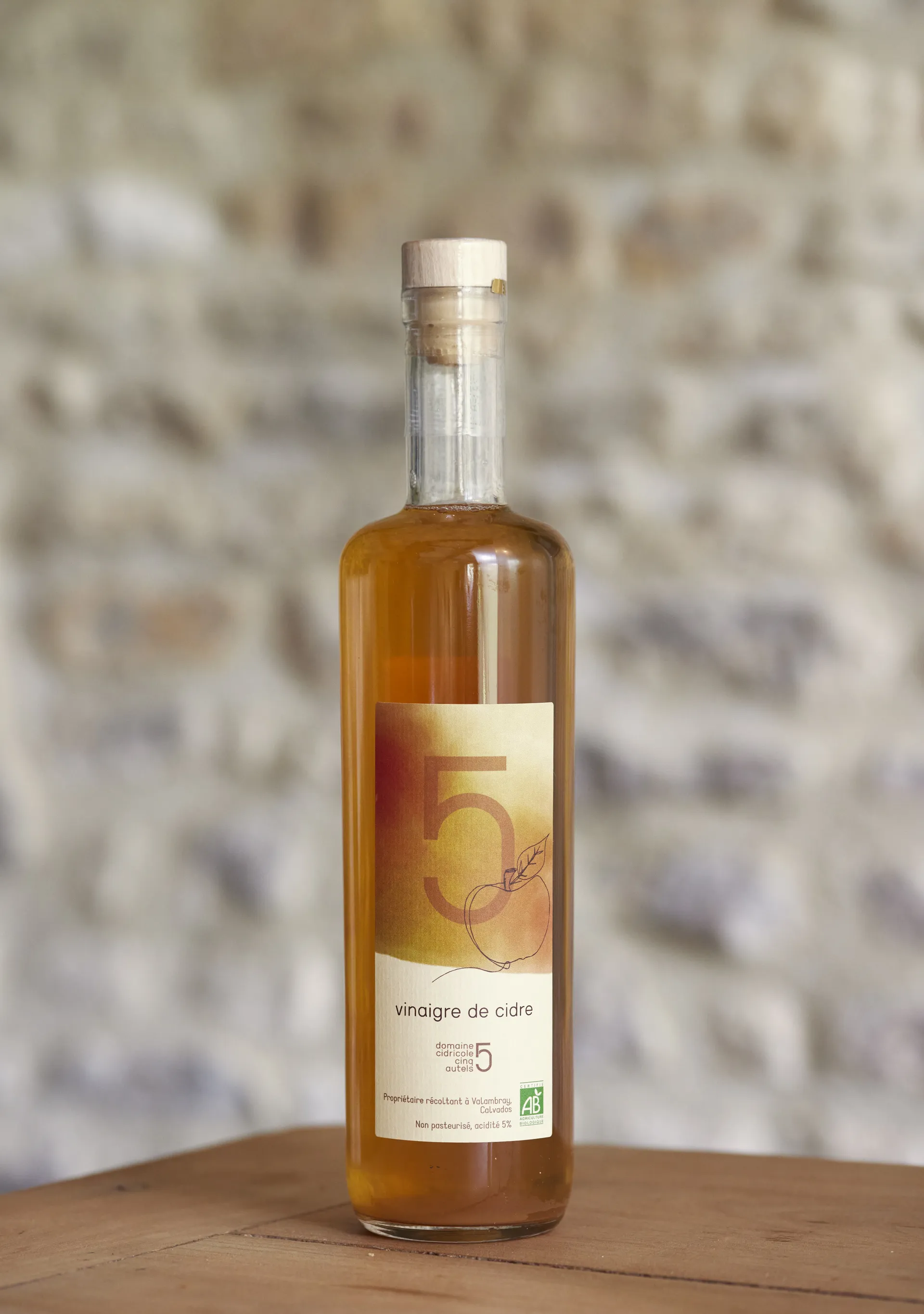 Bouteille de vinaigre de cidre du Domaine des Cinq Autels, sujet centré sur fond brique clair