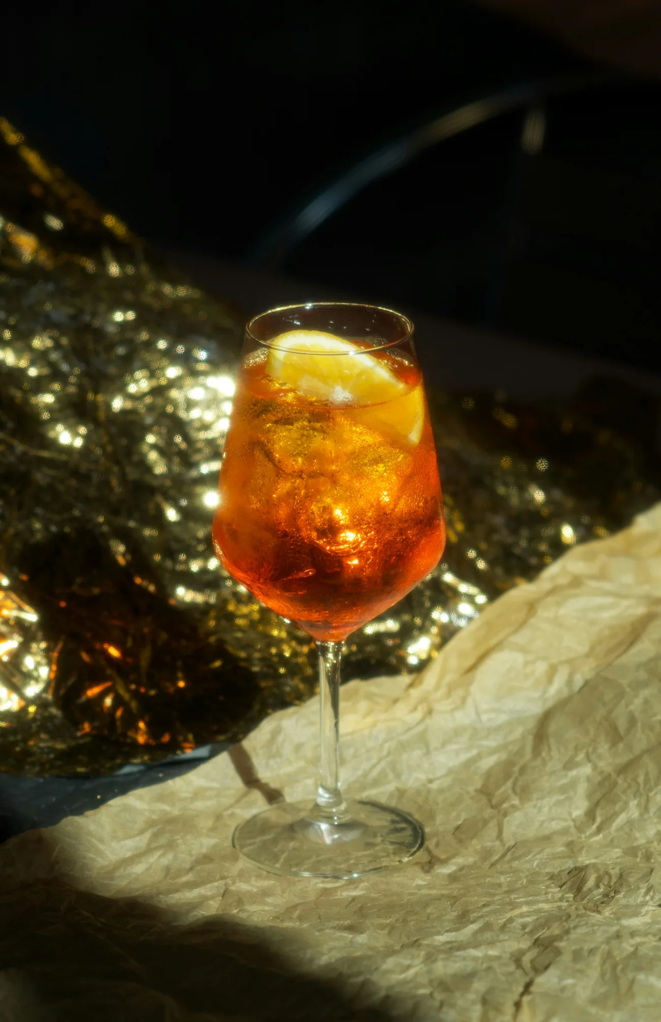 Spritz naranja helado en copa de vino, rodaja de cítrico y luces doradas