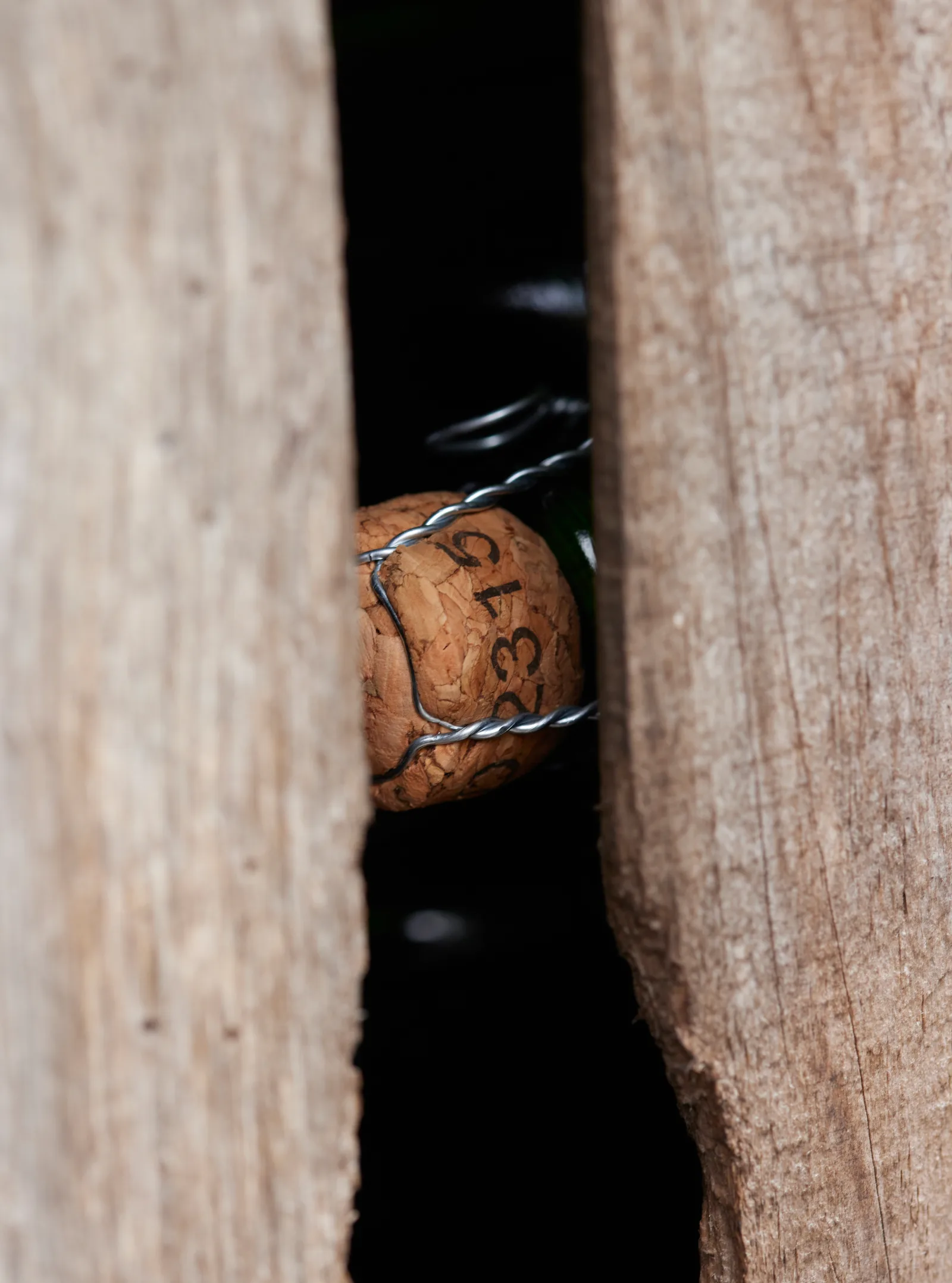 Tapón con bozal metálico de una botella de sidra visto a través de listones de madera, crianza en la bodega del Domaine des Cinq Autels