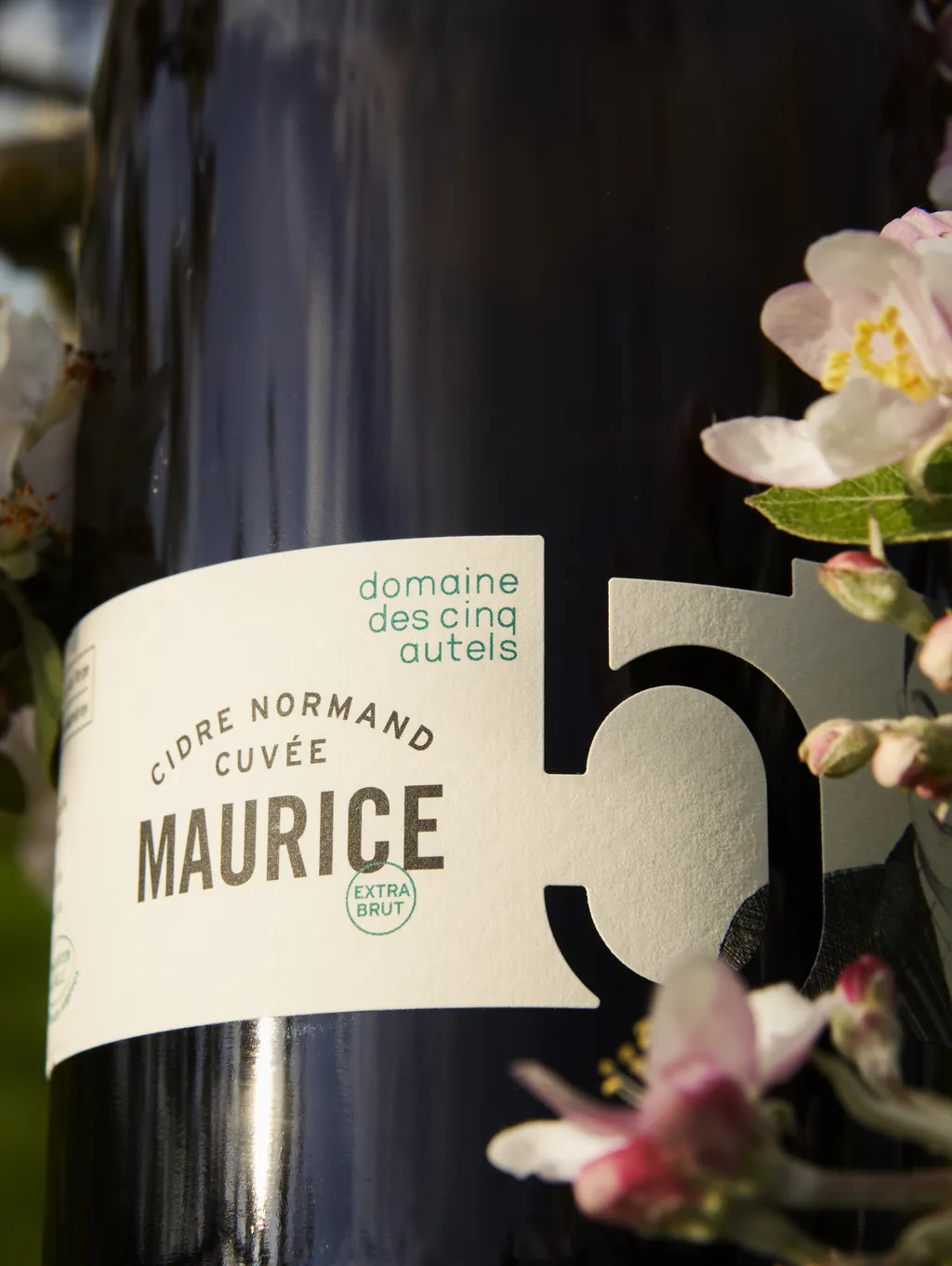 Etiqueta de la cuvée Maurice del Domaine des Cinq Autels sobre su botella retornable, entre flores de manzano